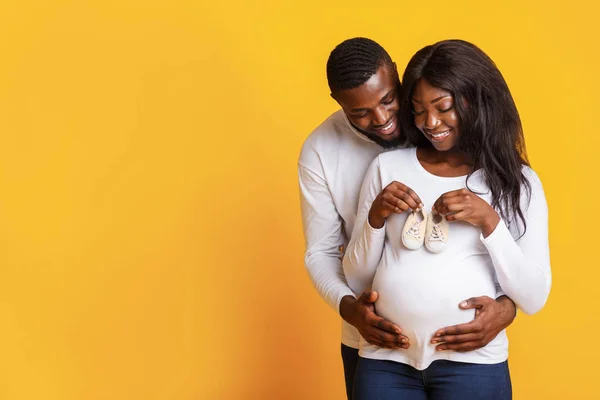 Casal grávida segurando suas futuras botas de bebê sobre fundo amarelo — Fotografia de Stock