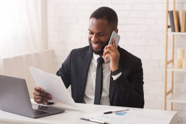 Mutlu Afrikalı işadamı raporları kontrol ediyor, asistanıyla telefonla konuşuyor.