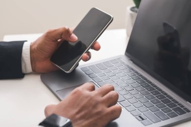 İşadamı boş ekranlı akıllı telefon kullanıyor ve laptop üzerinde çalışıyor