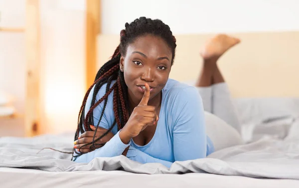 Mujer sosteniendo el dedo en los labios acostada en la cama en casa —  Fotos de Stock