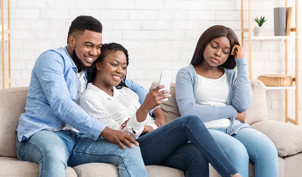 Chica negra celosa sentada cerca de una pareja romántica en el sofá, sentirse triste —  Fotos de Stock