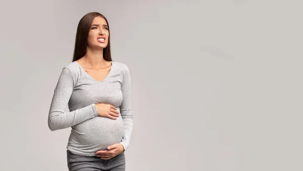 Dame enceinte souffrant de douleur à l'abdomen debout, fond gris, panorama — Photo