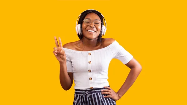 Zwart meisje in hoofdtelefoon Gesturing V-Sign Staande over gele achtergrond — Stockfoto