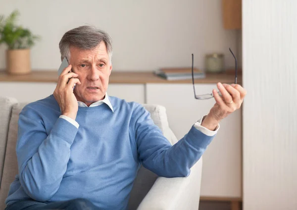 Старший джентльмен разговаривает по телефону сидя на диване дома — стоковое фото
