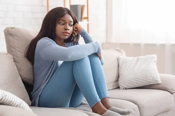 Mujer afroamericana deprimida y solitaria sentada en el sofá en casa —  Fotos de Stock