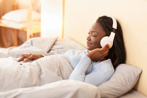 Señora en los auriculares escuchando audiolibro acostado en la cama interior —  Fotos de Stock