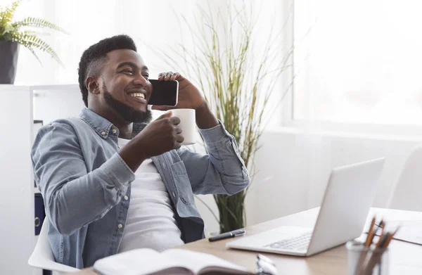 Negro hombre de negocios tomando un café y tomando el teléfono en la oficina —  Fotos de Stock