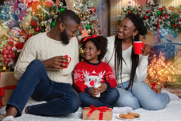 Cheerful african family eating snacks and drinking milk near Christmas tree