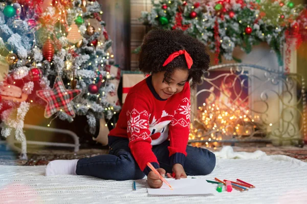 Doce menina escrevendo carta para Papai Noel na sala de estar decorada — Fotografia de Stock