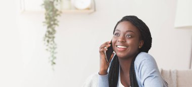 Neşeli Afrikalı Amerikalı kız evde cep telefonuyla konuşuyor.