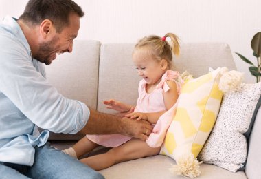 Mutlu baba küçük kızını koltukta gıdıklıyor.