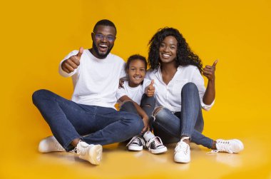 Neşeli Siyahi Aile Portresi Sarı Arkaplanda Baş Parmakla İşaret Ediyor