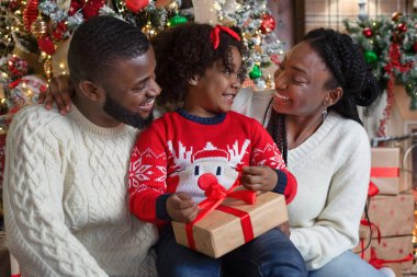 Küçük afro kız ailesiyle birlikte Noel hediyesi kutusunu açıyor.