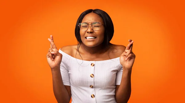 Fekete Y-generációs lány gazdaság ujjak keresztbe álló narancssárga háttér — Stock Fotó