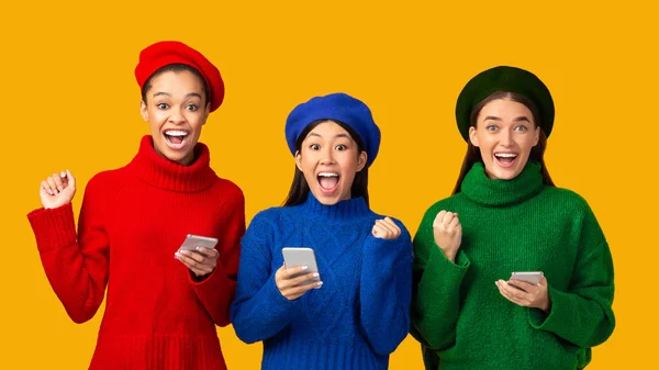 Tres chicas emocionadas sosteniendo Smartphones Gestos Sí sobre fondo amarillo — Foto de Stock