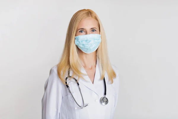 Женщина-врач в маске и со стетоскопом на сером фоне — стоковое фото