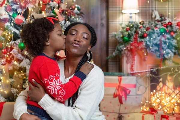 Loving afro mom and daughter kissing, congratulating each other with Christmas