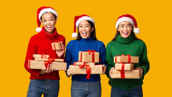 Tři různé dívky drží vánoční dárky stojící, žluté pozadí, Panorama — Stock fotografie