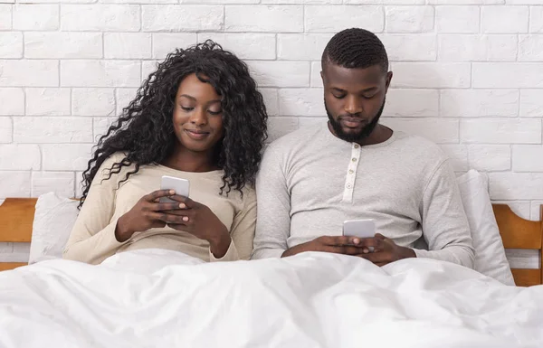 Junges afrikanisches Paar nutzt Smartphones im Bett und ignoriert sich gegenseitig — Stockfoto