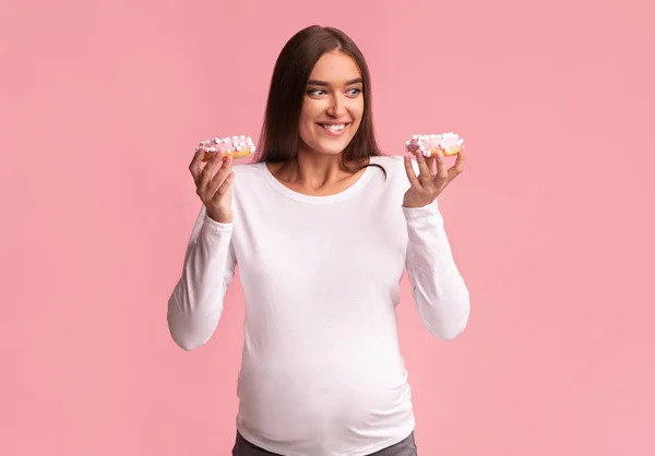 Fille enceinte tenant des beignets debout sur fond rose, Studio Shot — Photo