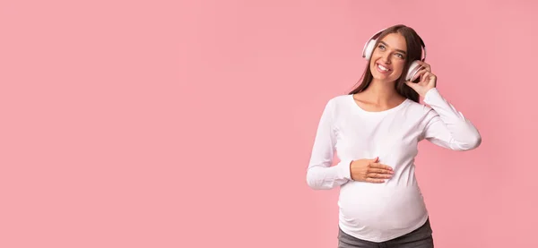 Femme enceinte positive appréciant la musique dans les écouteurs, fond rose, Panorama — Photo