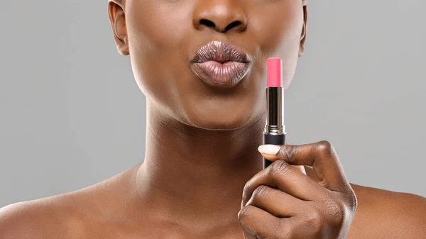 Black woman holding pink lipstick and pouting lips over grey background — Stock Photo, Image