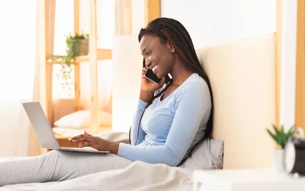 Черная леди разговаривает по телефону, сидя на кровати — стоковое фото