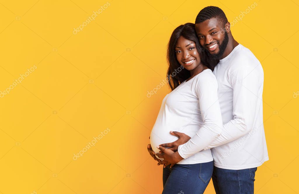 Pregnant afro woman and her husband embracing over yellow background