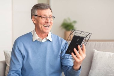 Son sınıf öğrencisi elinde fotoğraf çerçevesiyle evdeki koltukta oturuyor.