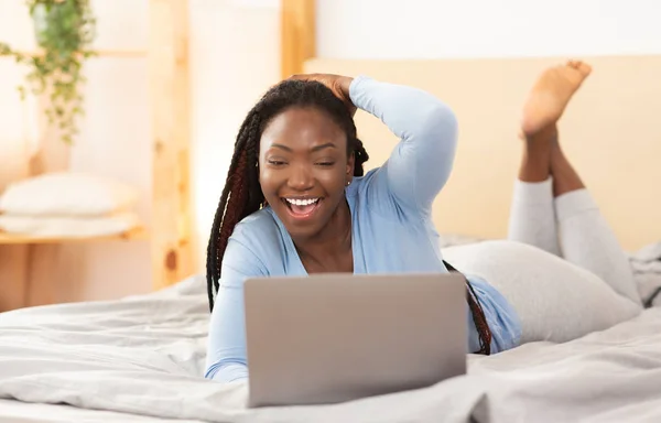 Afro ragazza fare video chiamata via computer portatile sdraiato a letto — Foto Stock