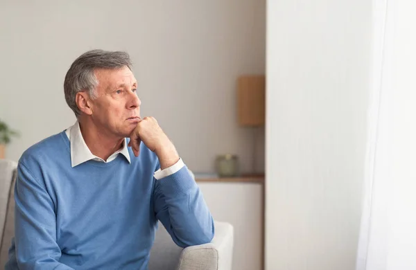 Расстроенный старший джентльмен сидит на диване дома после выхода на пенсию — стоковое фото
