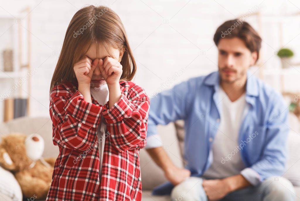 Little girl crying after arguing wIth dad, angry father behind