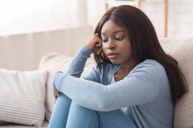 Üzgün siyah kız, düşünceli yüz ifadesiyle kanepede oturuyor.