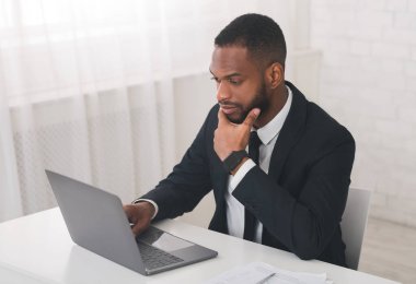 Ofiste dizüstü bilgisayarla çalışan düşünceli iş adamı.