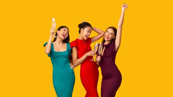 Tři dívky slaví pití šumivé víno a tanec, žluté pozadí — Stock fotografie