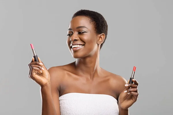 Wanita afro ceria memegang dua lipstik, memilih warna yang tepat — Stok Foto