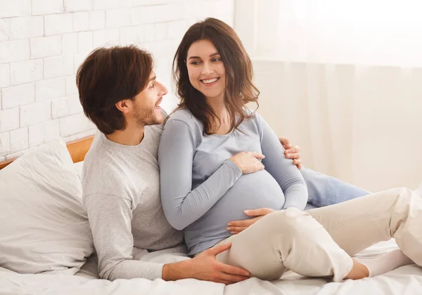 Glad gravid par avkopplande på sängen hemma tillsammans — Stockfoto