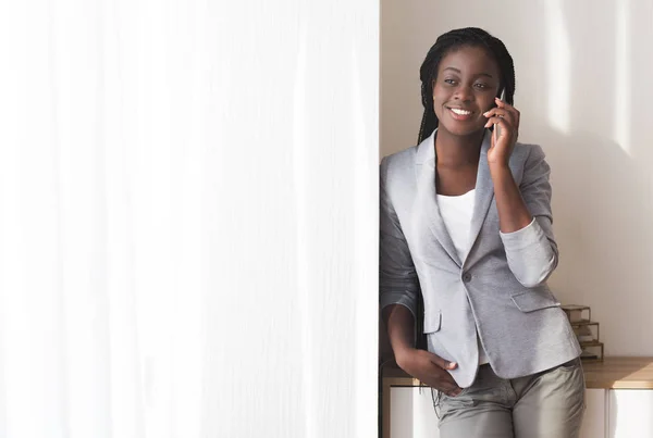 Черная деловая женщина разговаривает по мобильному телефону у окна в офисе — стоковое фото