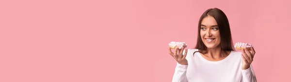 妊娠中の女性ピンクの背景に2つのドーナツを保持,パノラマ — ストック写真