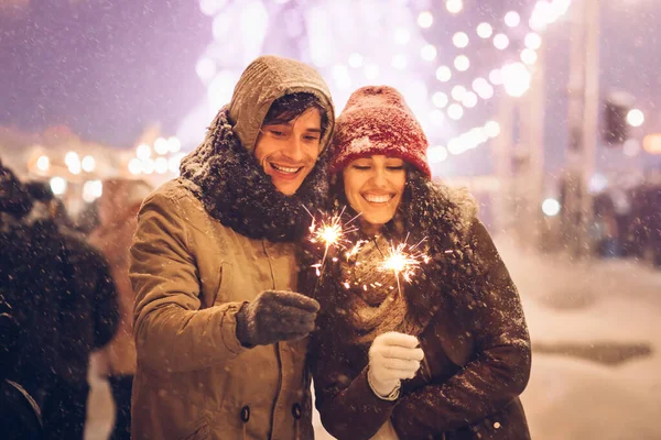 Alegre pareja sosteniendo luces de bengala Sparklers celebrando el año nuevo fuera —  Fotos de Stock