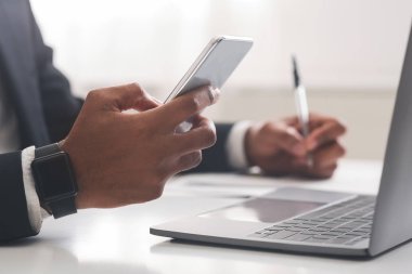 Afrika kökenli Amerikalı iş adamı akıllı telefon kullanıyor ve ofiste notlar alıyor.