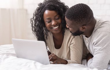 evde yatakta dizüstü kullanarak gülümseyen genç Çift