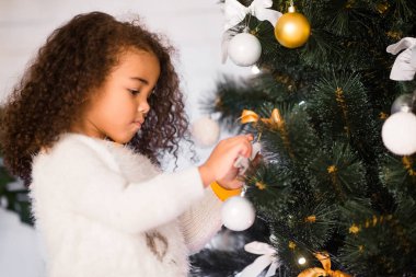 Odaklanmış Afrikalı küçük kız evde Noel ağacı süslüyor.