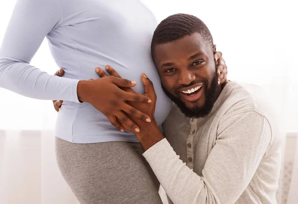 Marido feliz ouvindo sua barriga da esposa grávida em casa — Fotografia de Stock