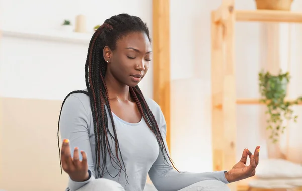 Relajada mujer afro meditando sentada en posición de loto en casa —  Fotos de Stock