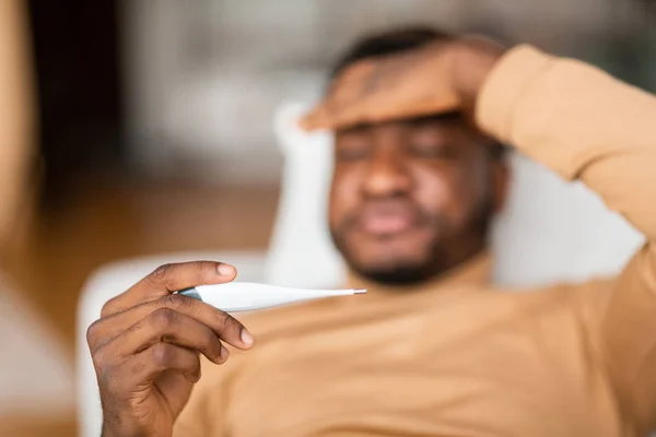 Tipo enfermo que mide la temperatura corporal con termómetro acostado en casa — Foto de Stock