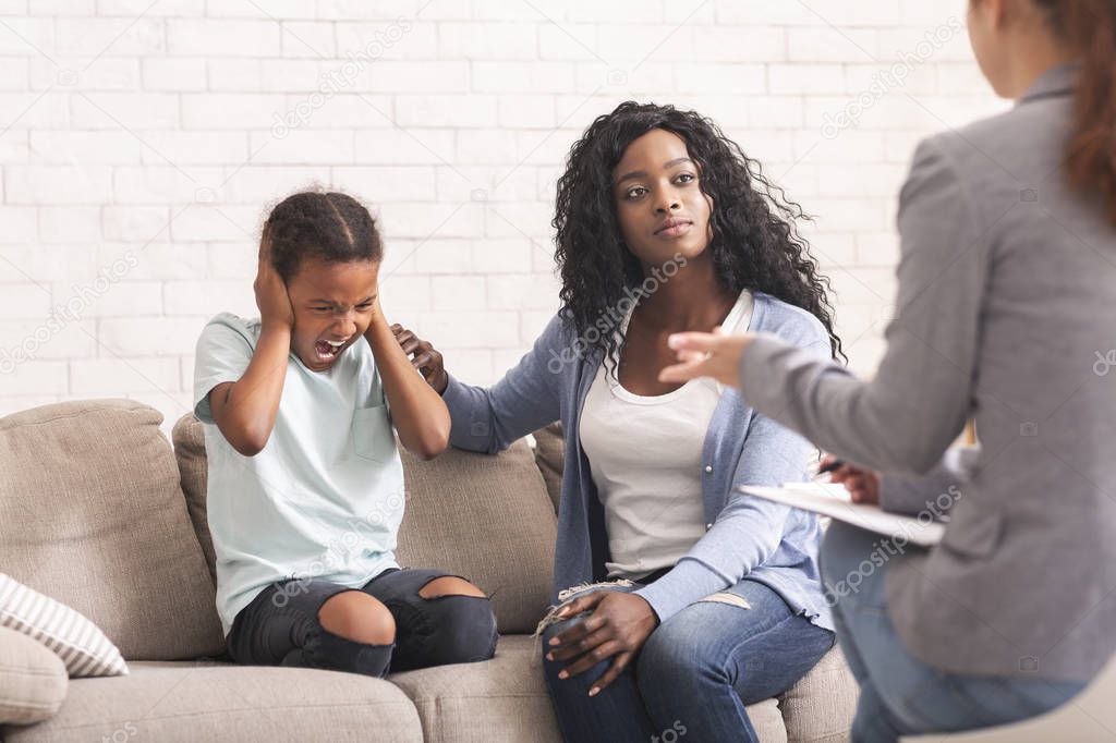 Caring black mother comforting her naughty little daughter at psychologist consultation