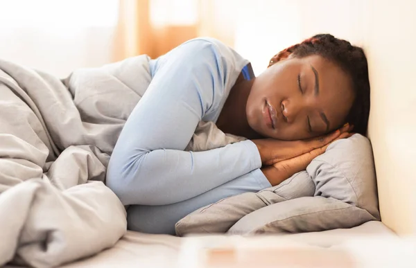 Negro chica durmiendo celebración plegado manos cerca cara en dormitorio —  Fotos de Stock
