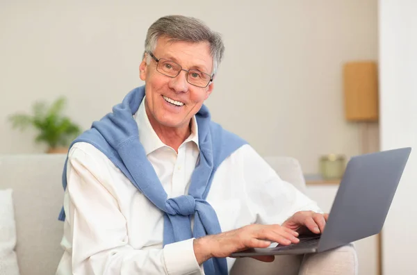 Senior Gentleman Χρησιμοποιώντας Laptop Χαμογελώντας κάθεται στον καναπέ — Φωτογραφία Αρχείου