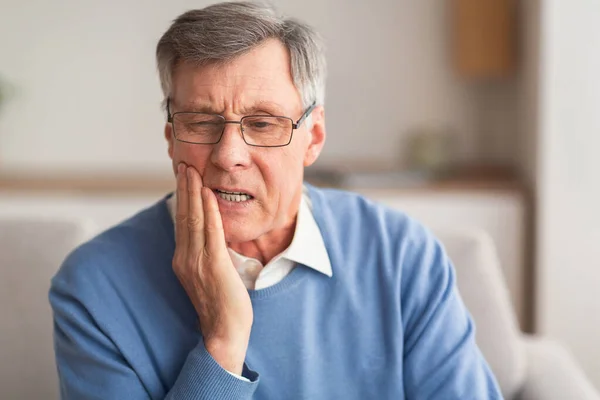 Homem idoso com dor de dente sentado no sofá em casa — Fotografia de Stock